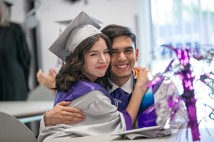 A teen girl and teen boy hug in their graduation caps and gowns
