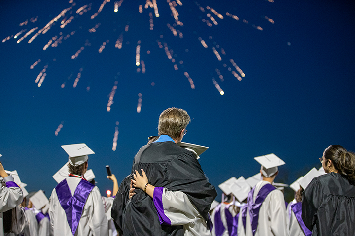 A graduate and her dad hug as fireworks explode in the background