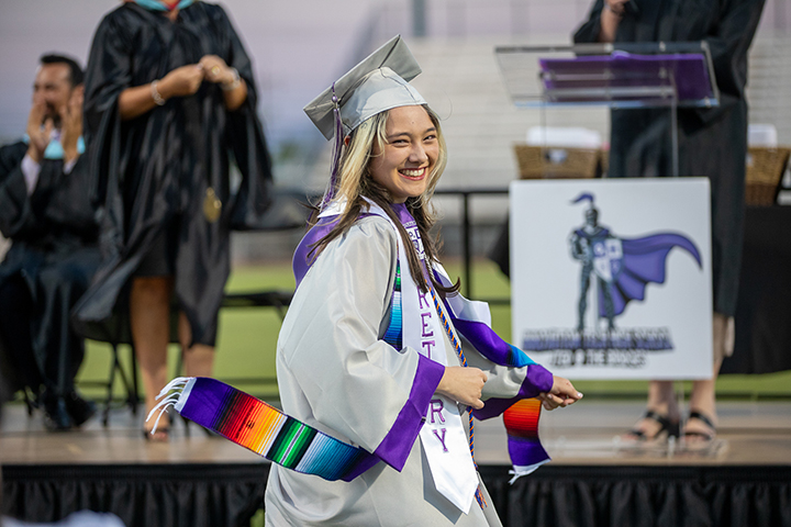 A graduate proudly walks across the field in her cap and gown