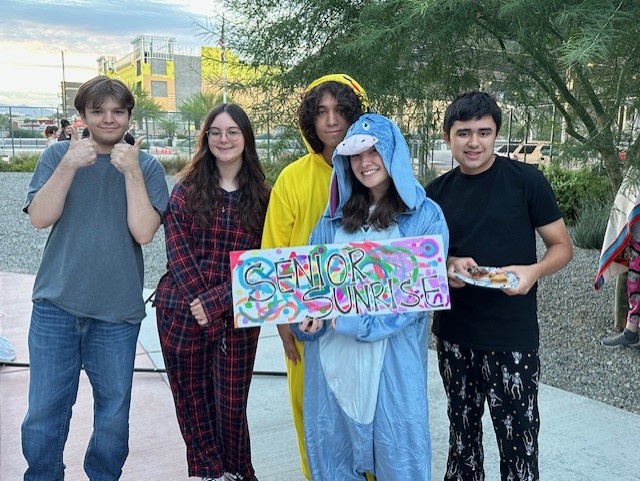 A group of friends pose with a Senior Sunrise banner