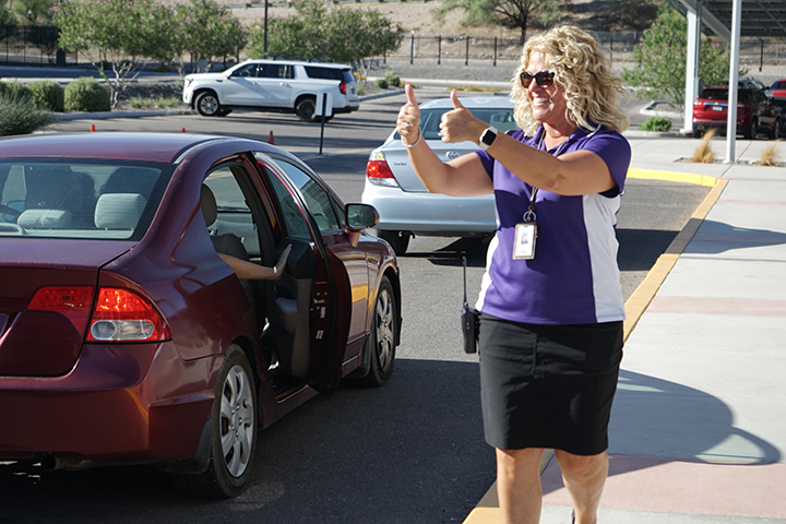 A woman in a purple shirt gives a thumbs up to cars in the dropoff line