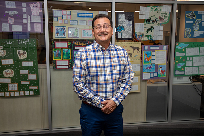 A man in a plaid shirt and glasses smiles in front of a case of student projects
