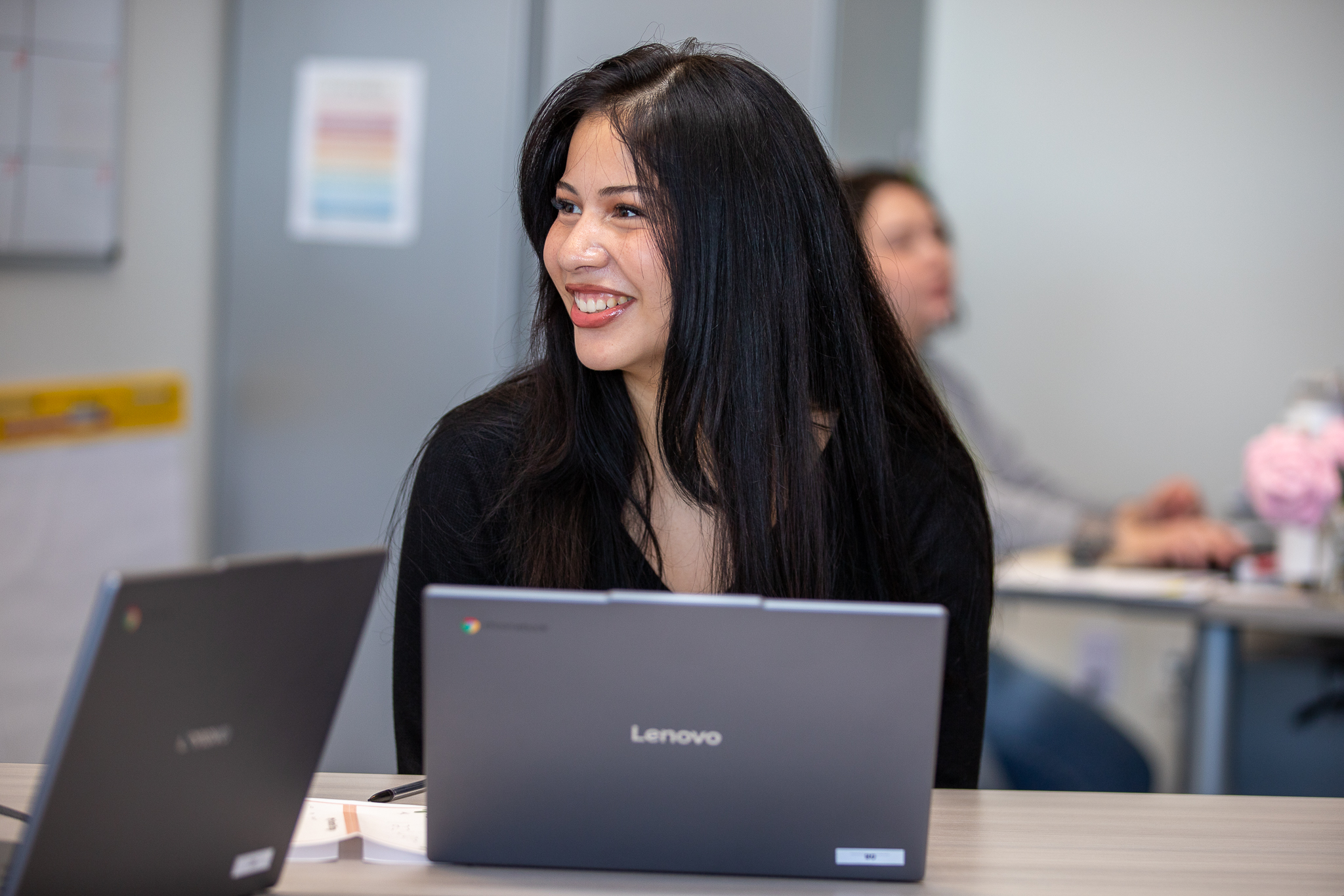 A teen girl smiles as she works on her laptop during class