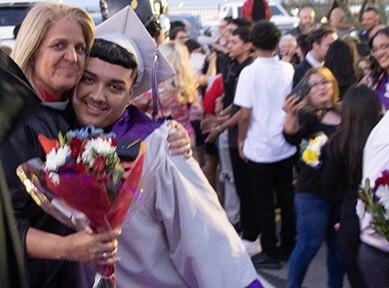 An InTech grad hugs his principal while holding a bouquet of flowers